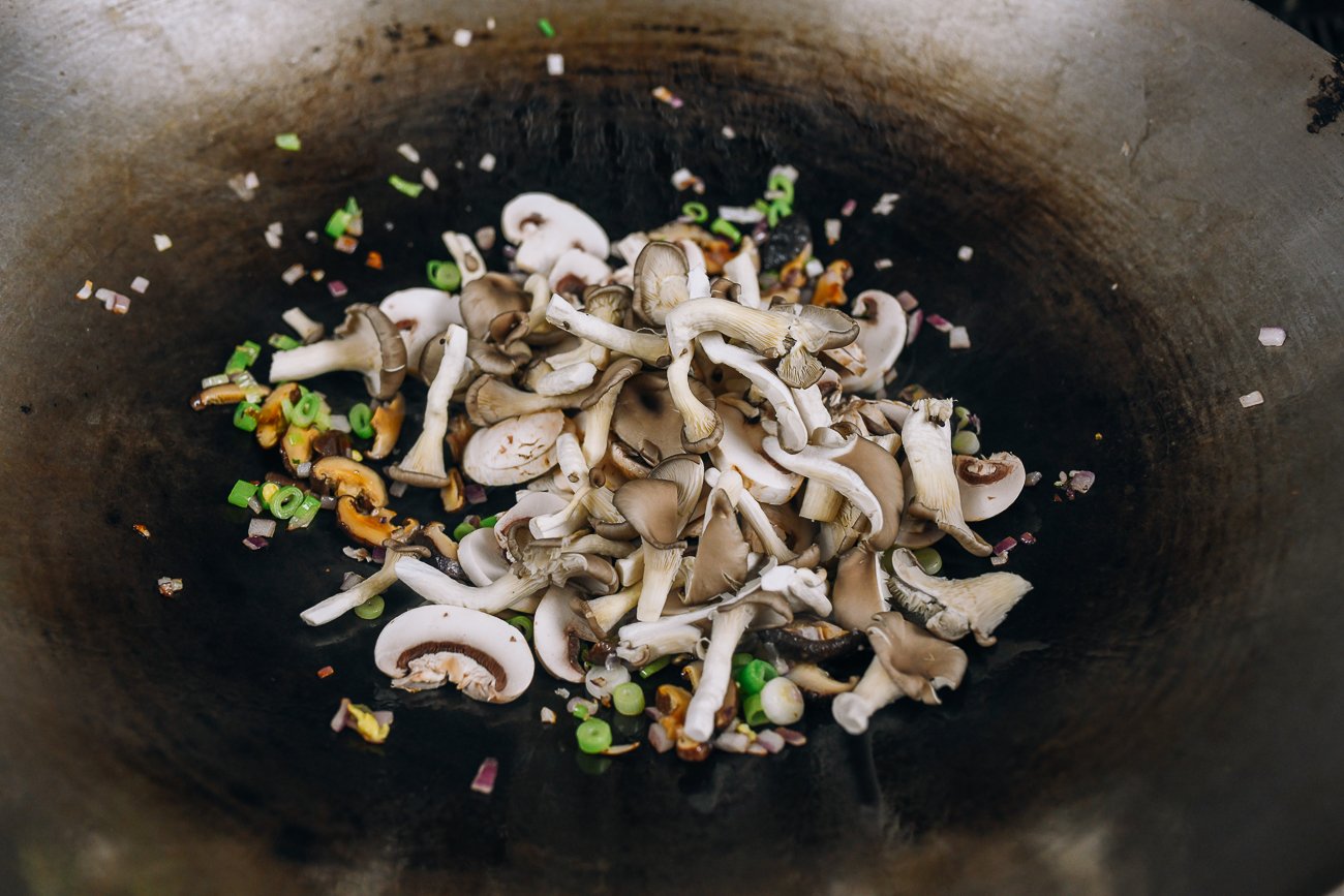 adding fresh mushrooms to wok