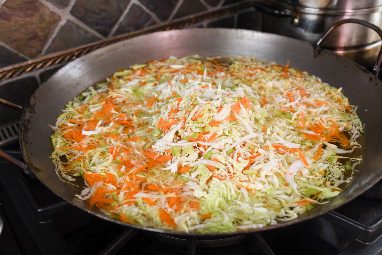 blanching shredded cabbage, carrots, and celery in large wok of boiling water