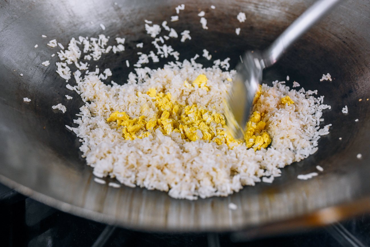 adding scrambled eggs to white rice in wok