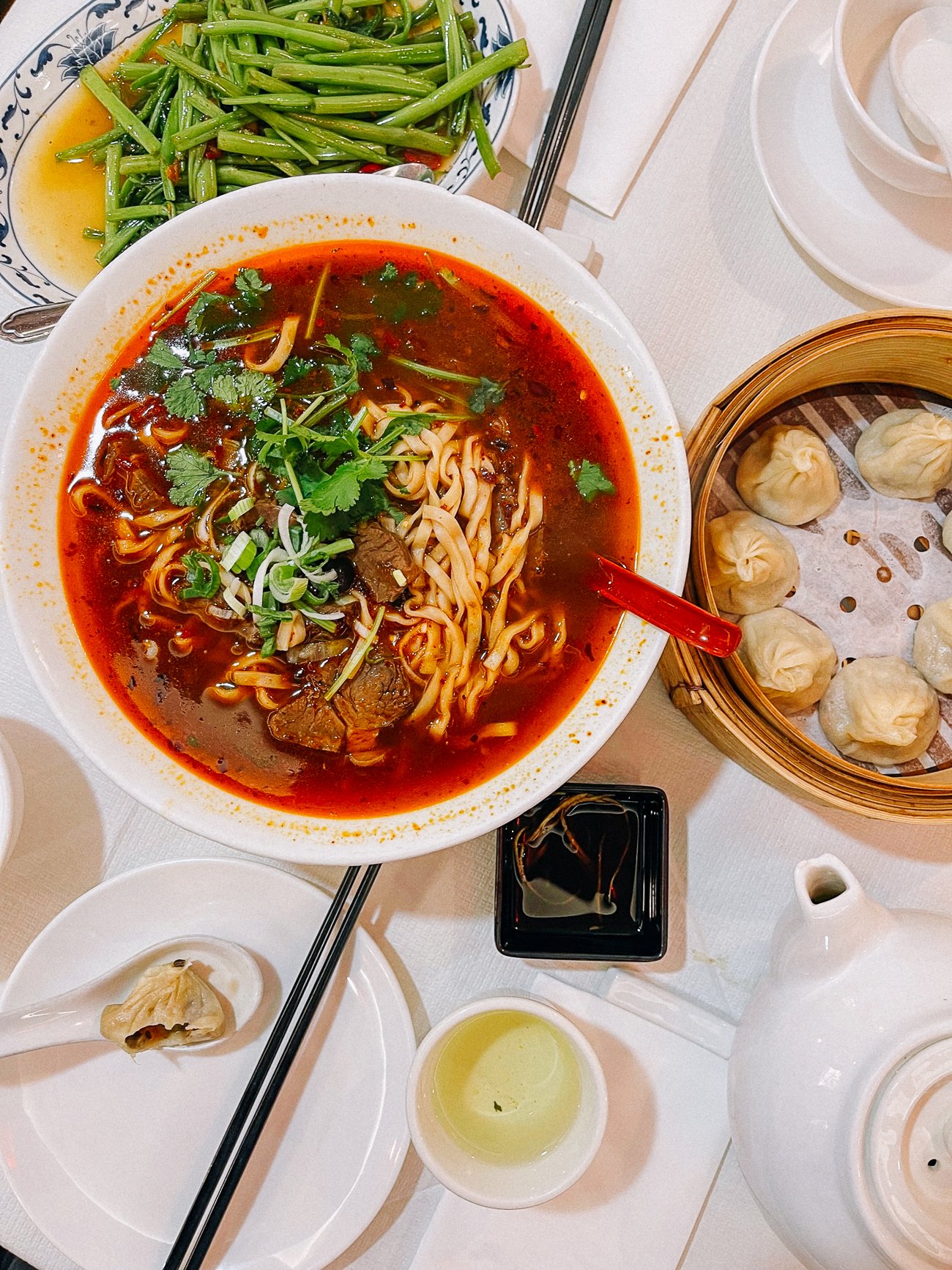 Bowl of spicy beef noodle soup and soup dumplings with tea and vegetables