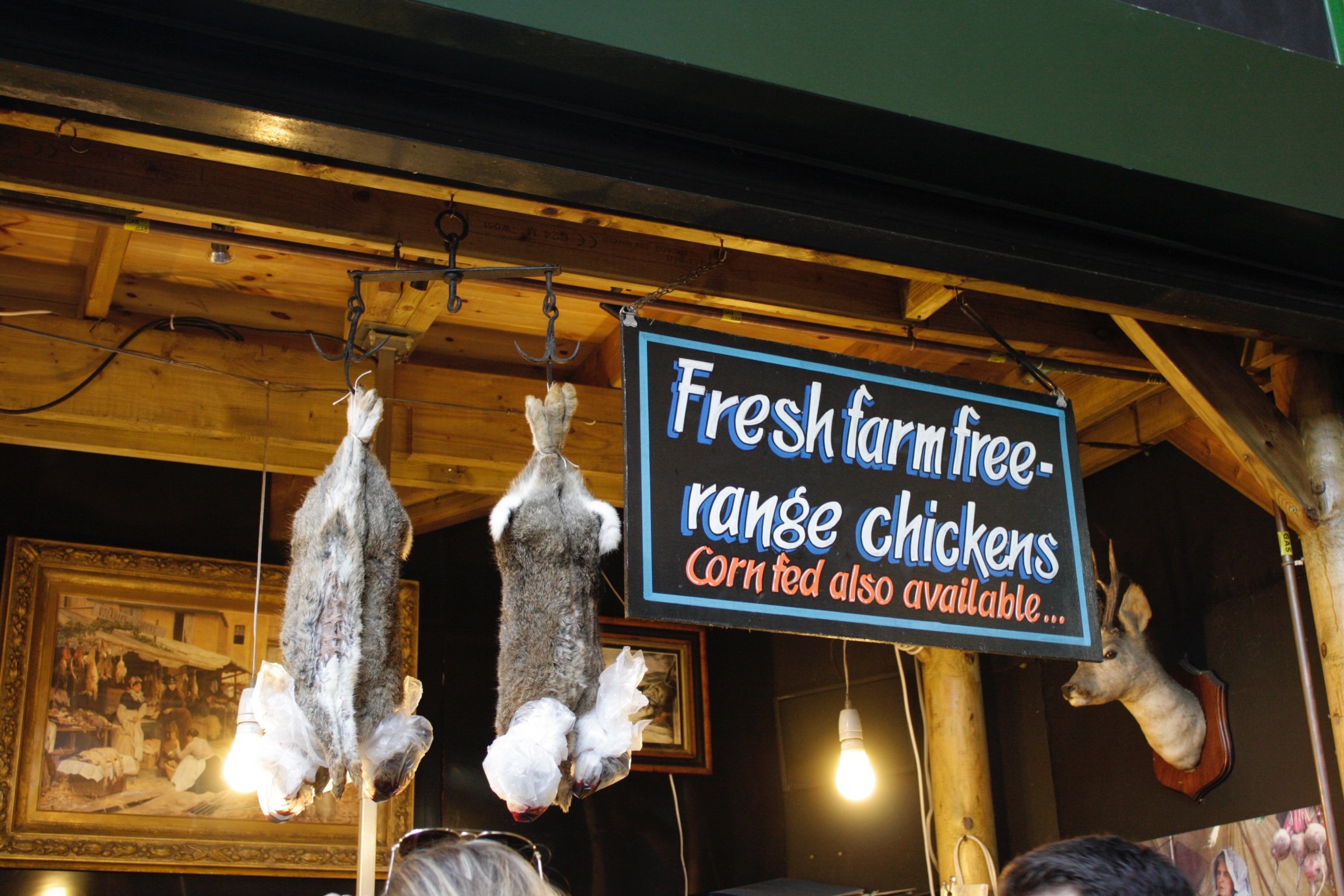 Game rabbits hanging next to a sign for fresh farm free-range chickens at Borough Market