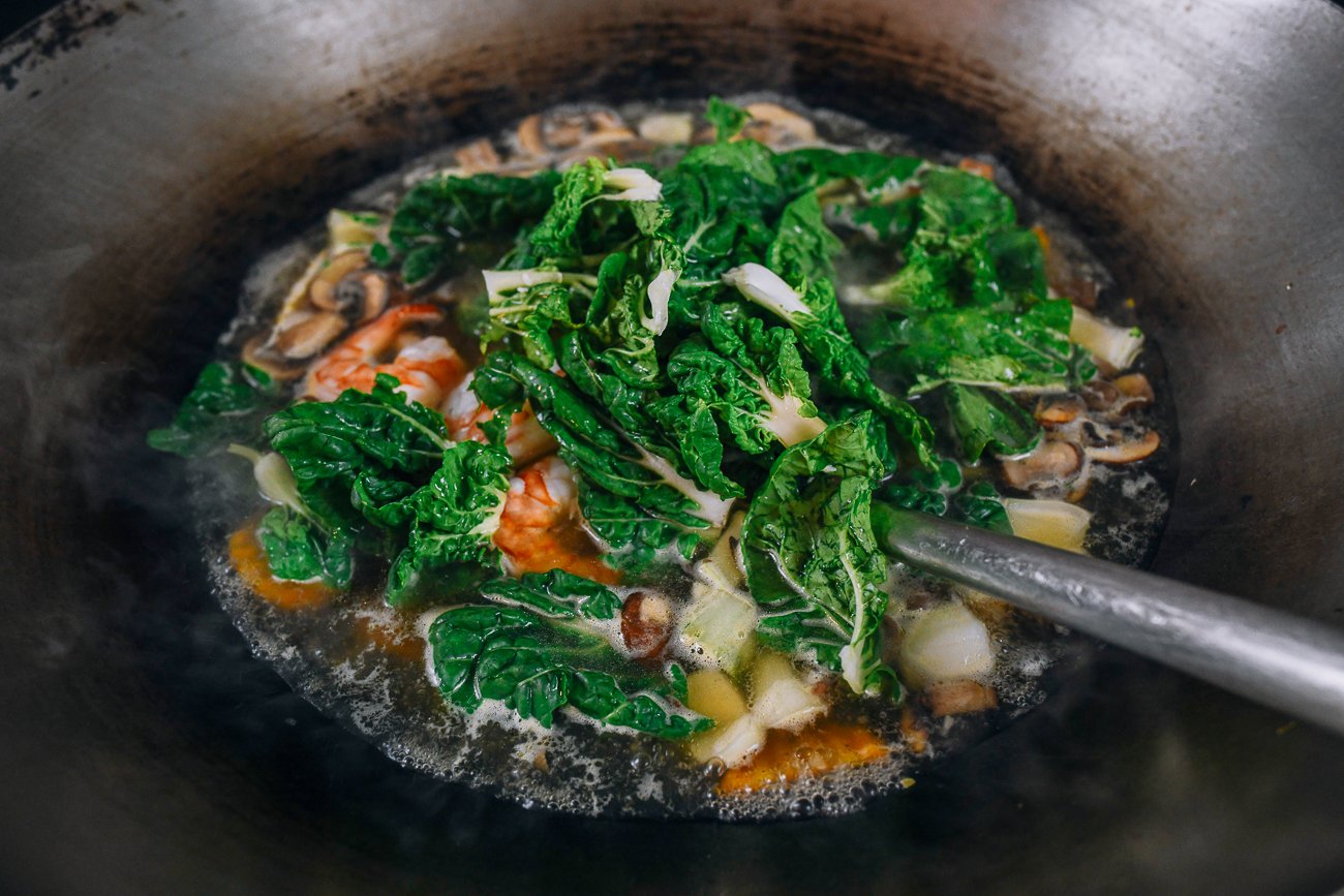adding bok choy leaves to soup in wok