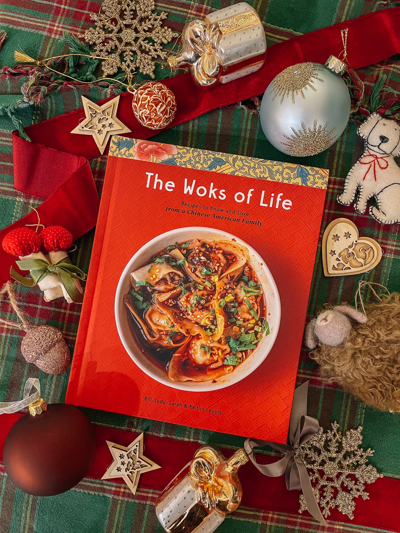 The Woks of Life Cookbook with cozy Christmas ornaments around it