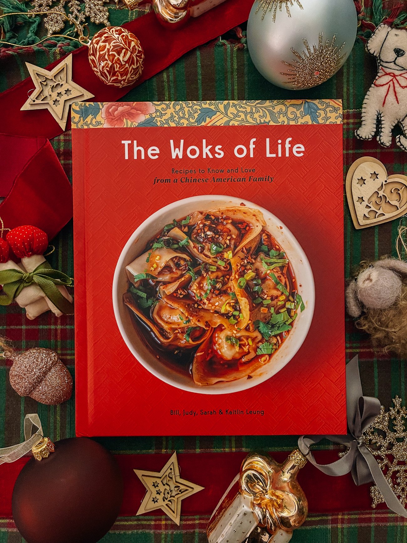 The Woks of Life Cookbook with cozy Christmas ornaments around it