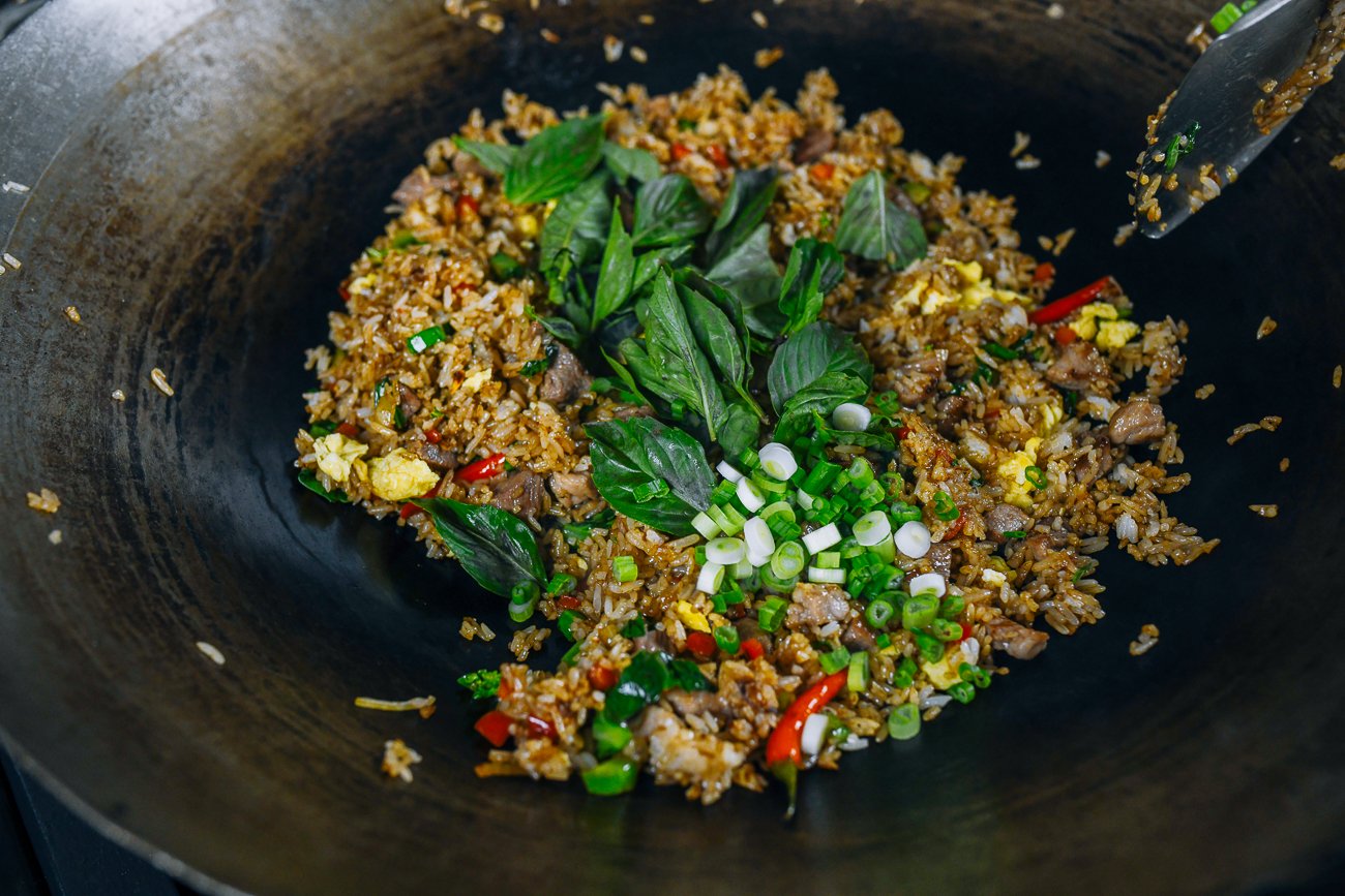 Thai basil and scallions added to Thai fried rice in wok
