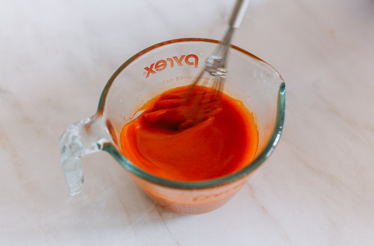 whisking hot sauce and melted butter together in a measuring cup
