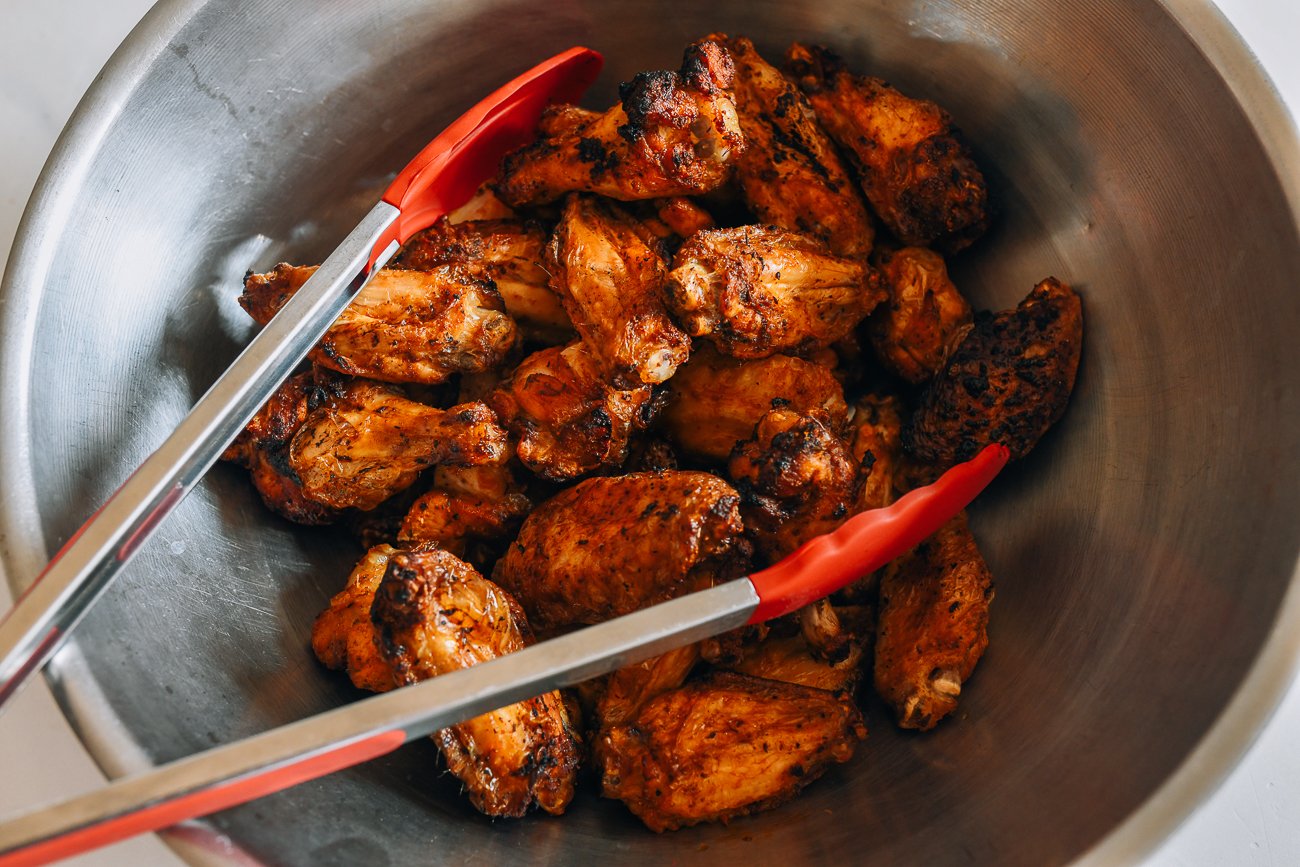 air fried chicken wings in steel mixing bowl with tongs