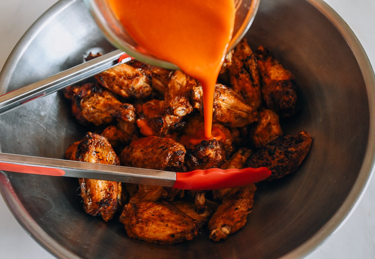 pouring hot sauce onto wings