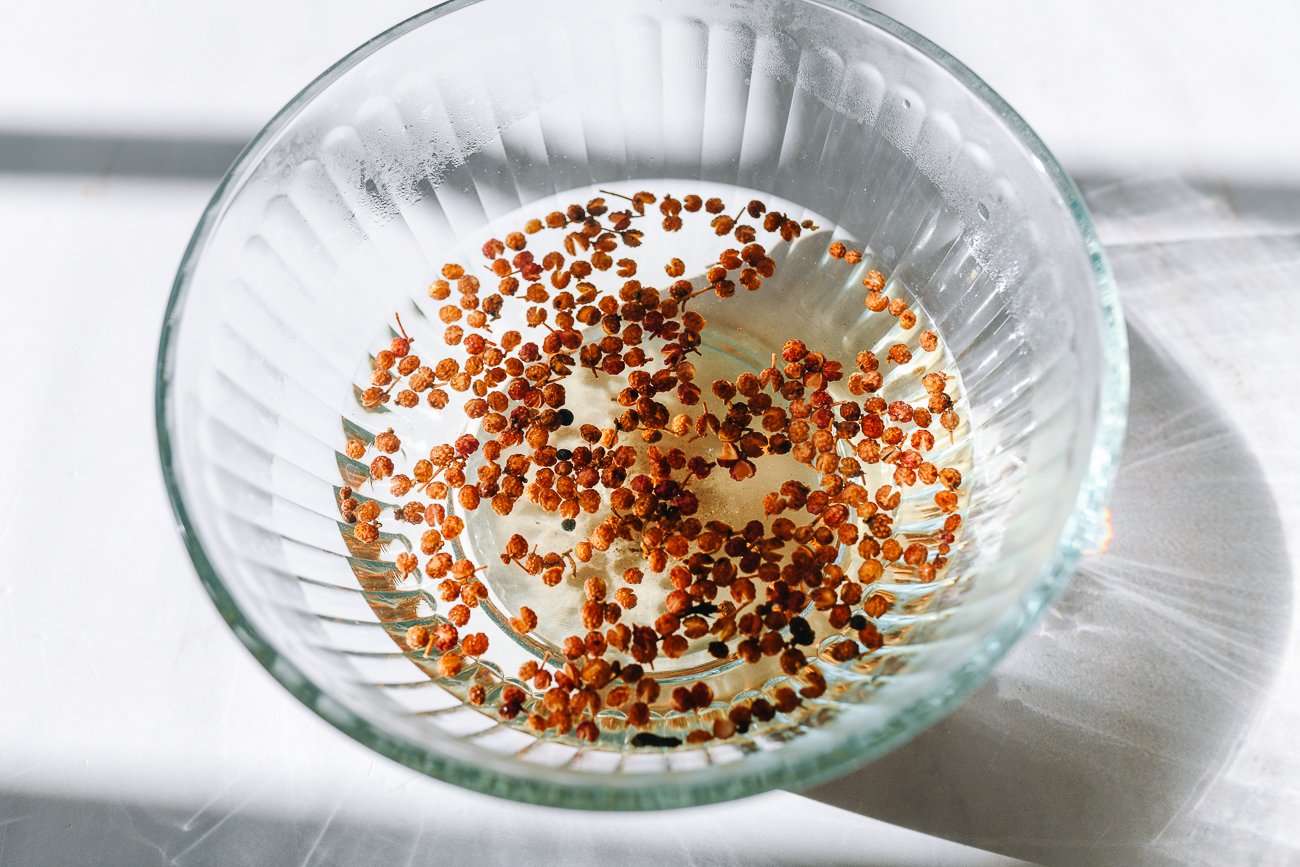 Sichuan peppercorns soaking in glass bowl of water