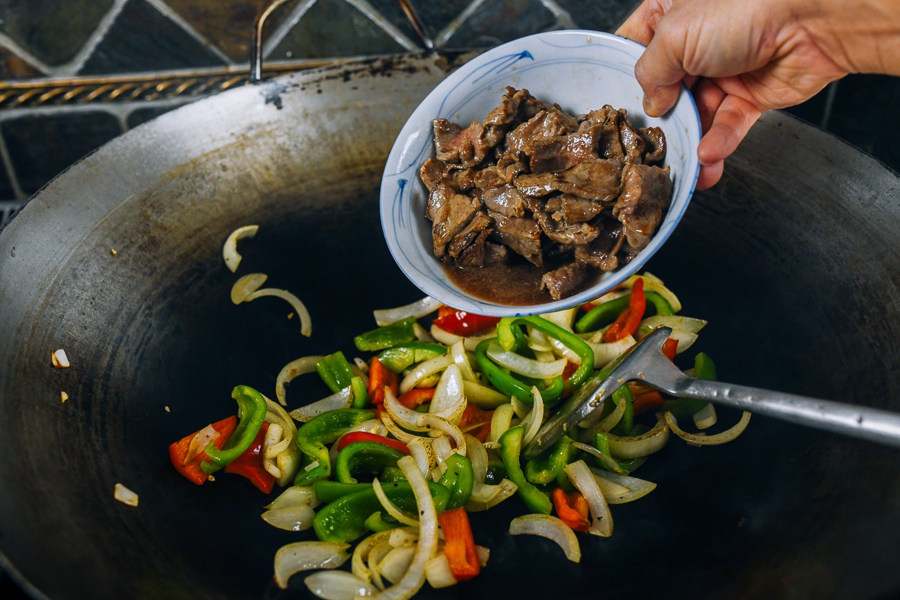 adding seared beef to vegetables in wok