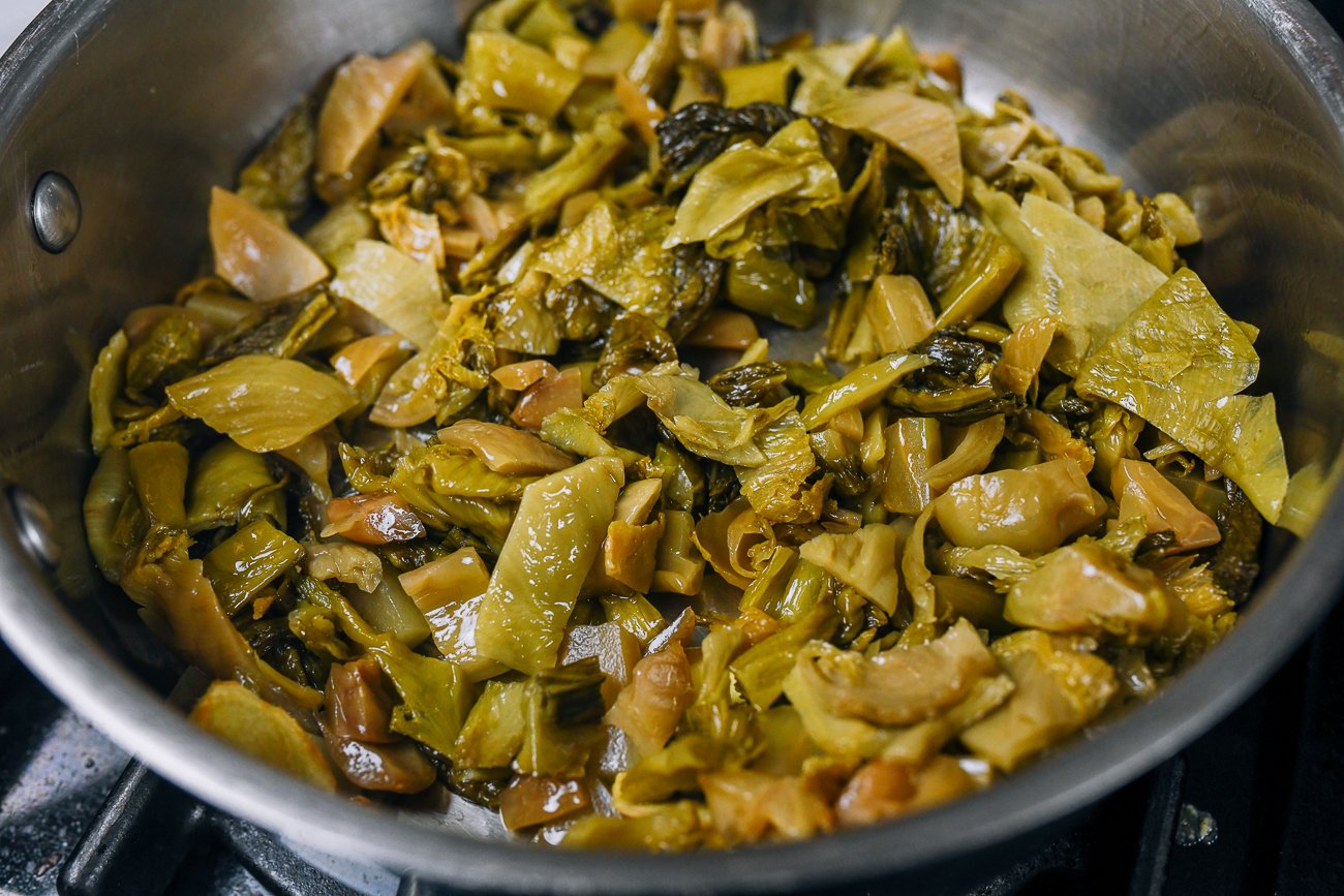 cooking chopped pickled mustard greens in a stainless steel skillet