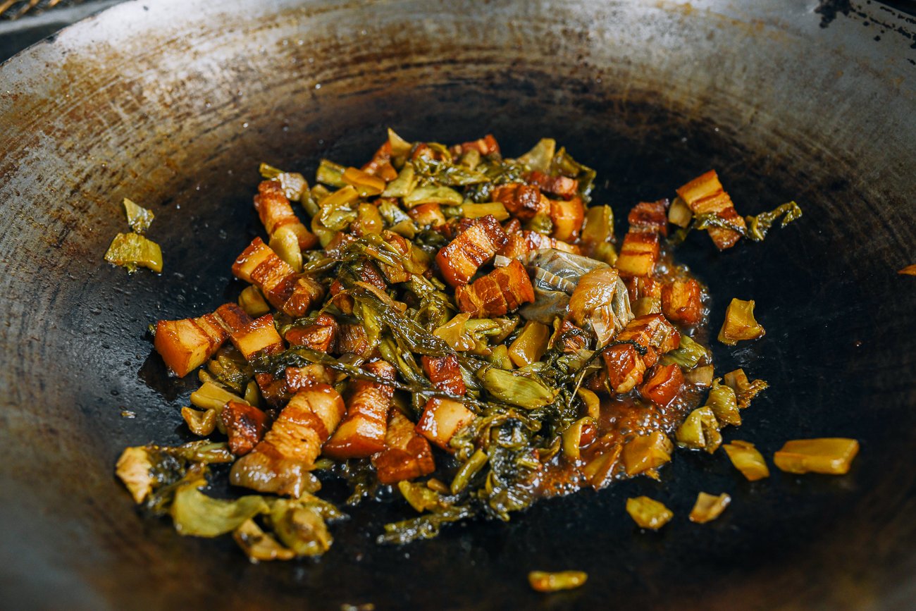 pork belly in wok with pickled mustard greens