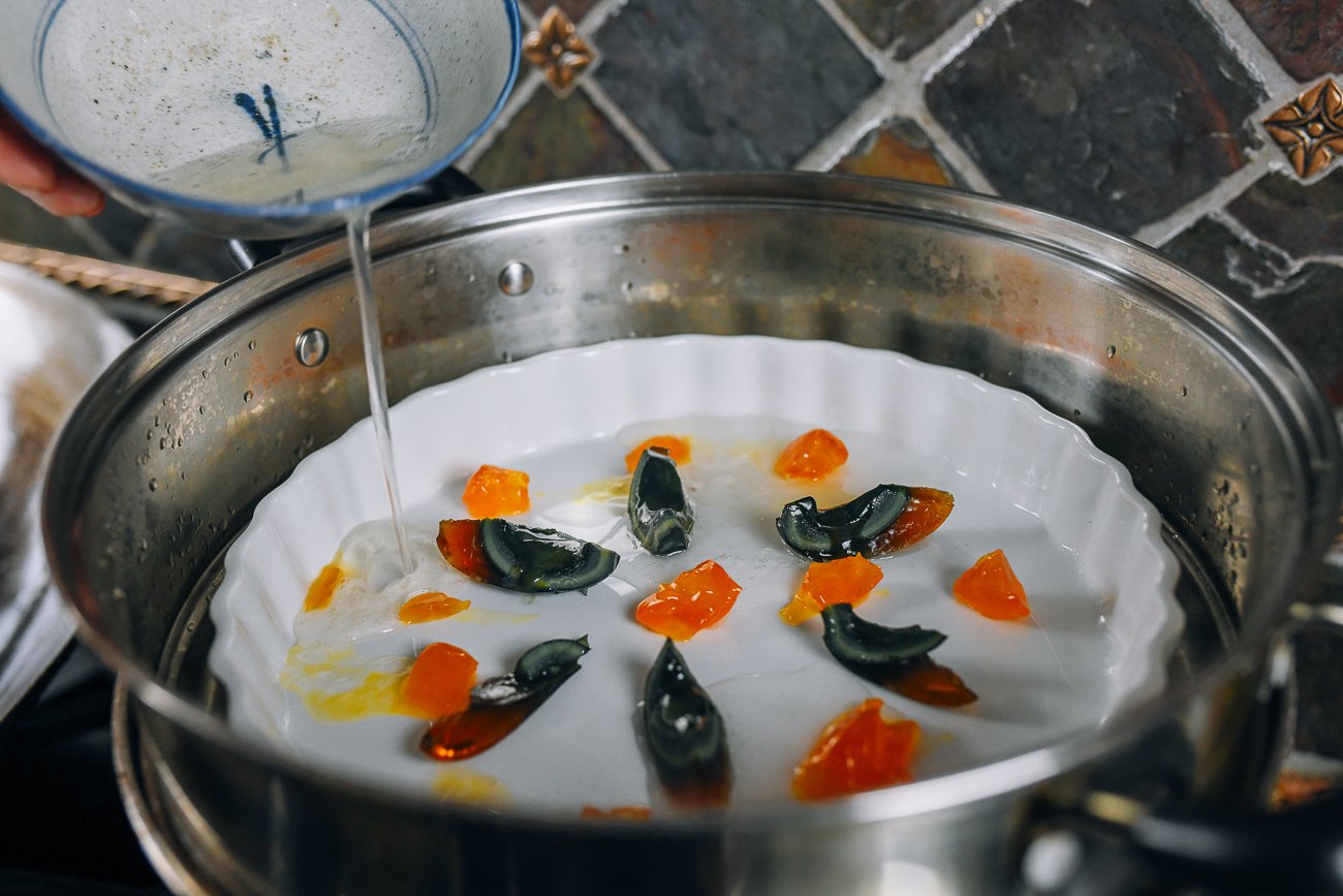 pouring salted duck egg white into dish with century egg and salted duck egg yolk