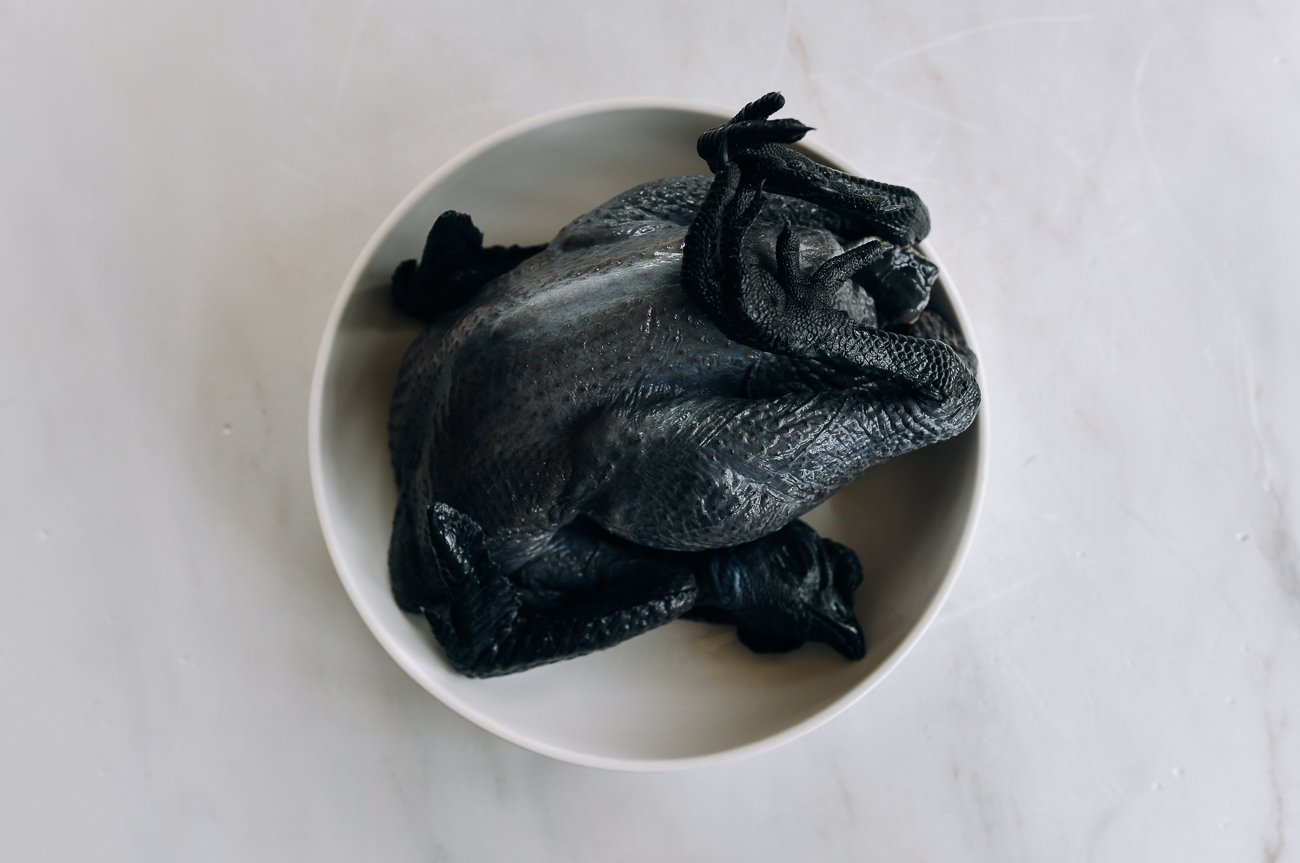 whole raw black chicken on plate