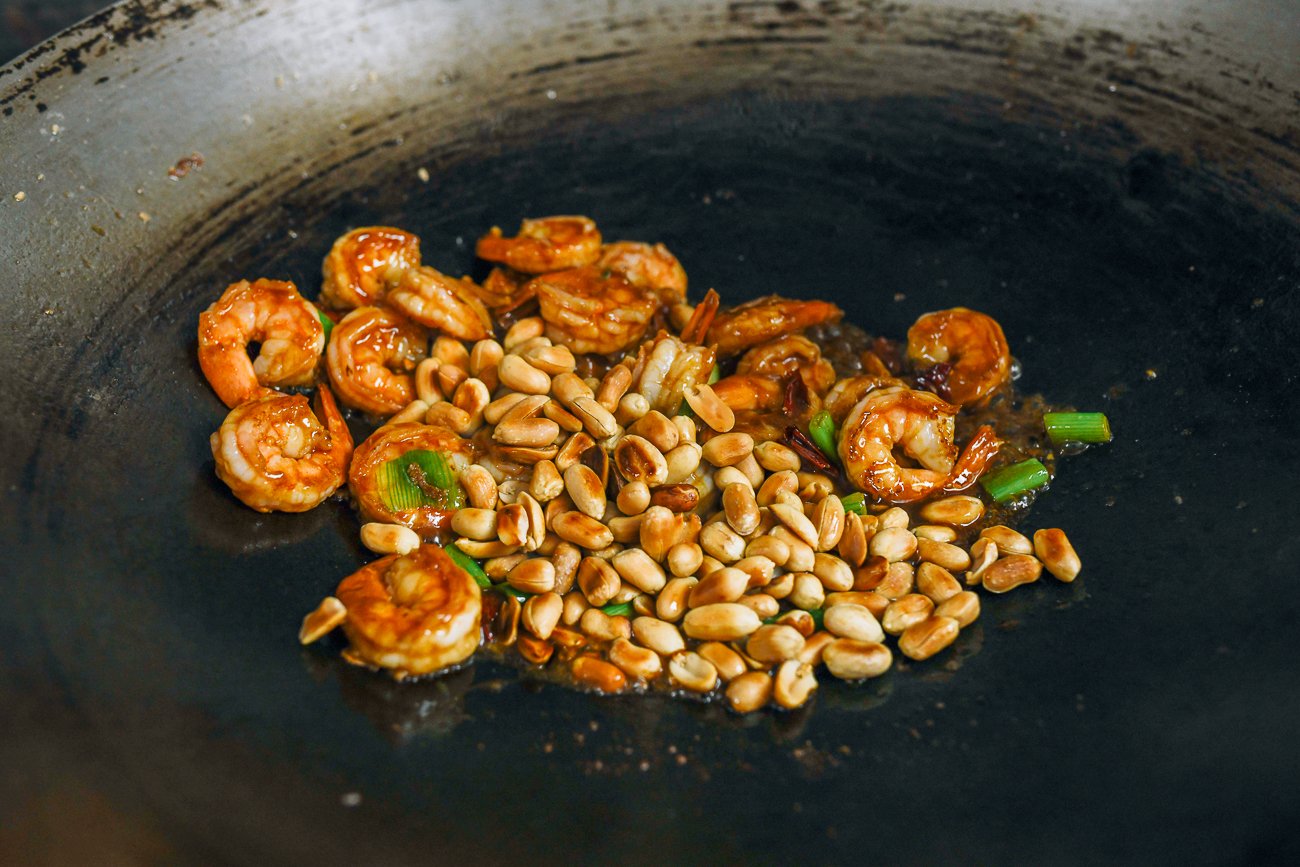 adding peanuts to shrimp in wok