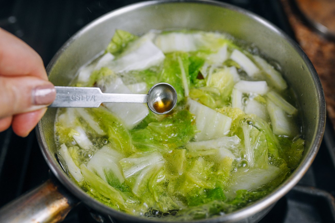 adding sesame oil to duck soup with napa cabbage