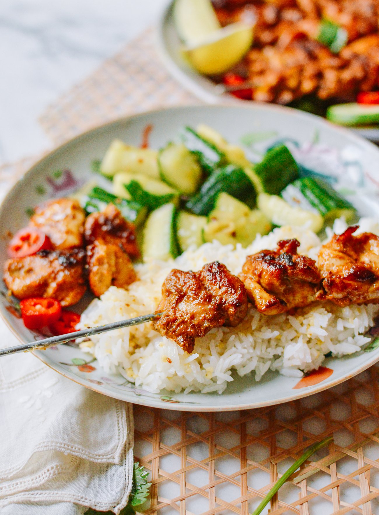 Chicken Satay skewer on plate with rice and raw cucumber