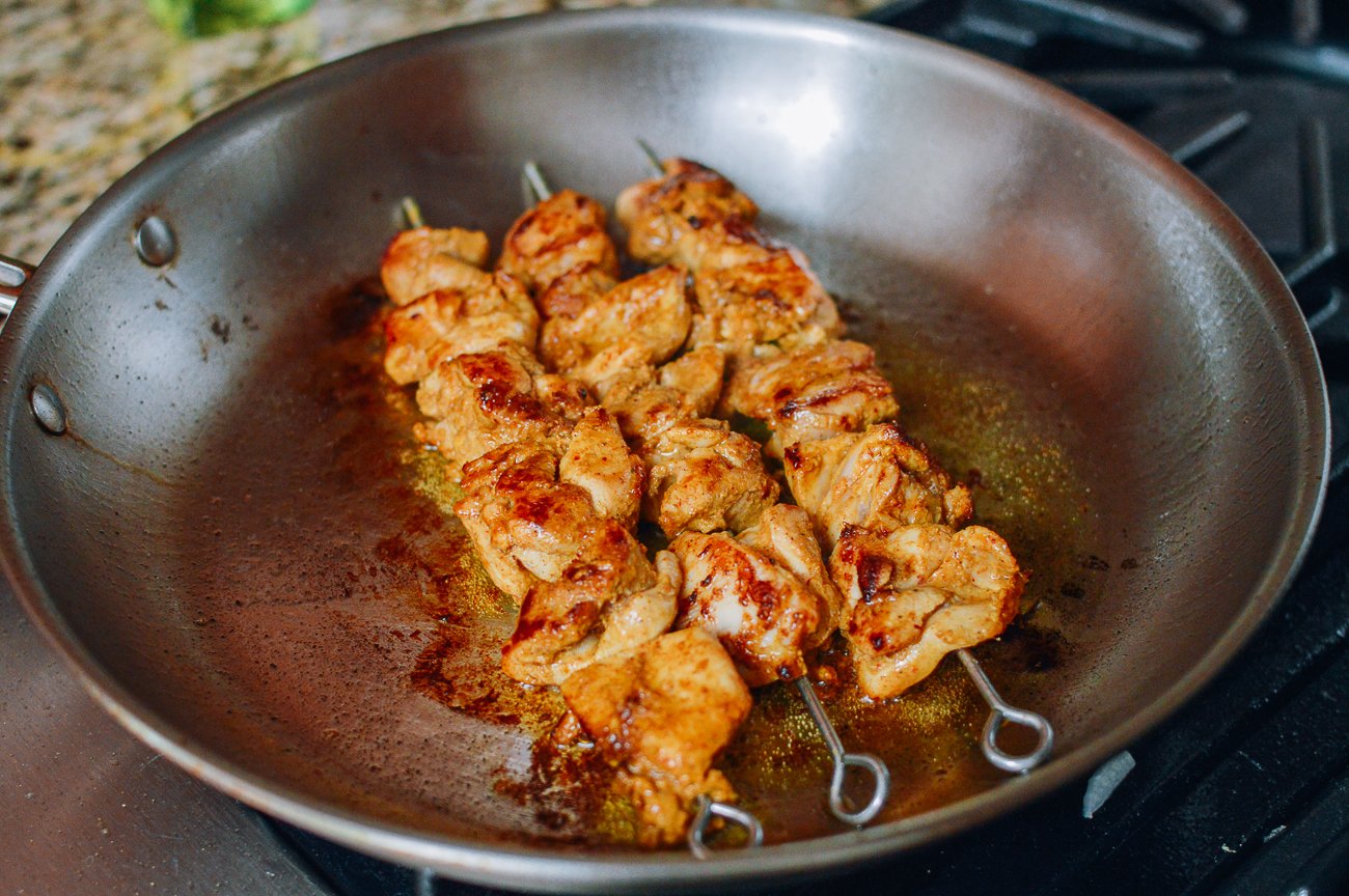 cooking chicken satay skewers in frying pan on stove