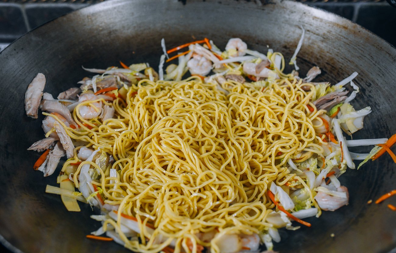 lo mein noodles added to other ingredients in wok
