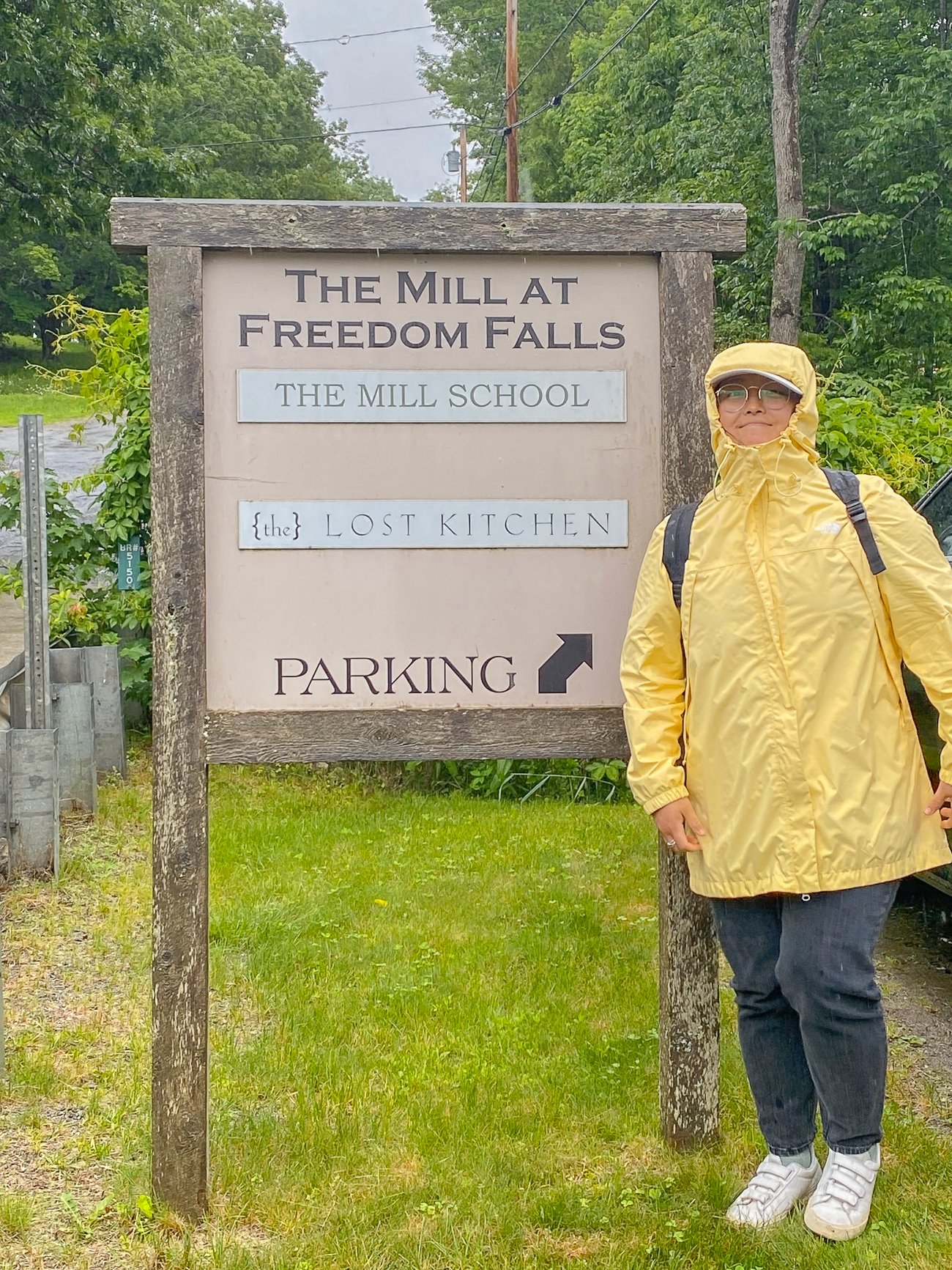 Kaitlin in a yellow raincoat by The Lost Kitchen sign