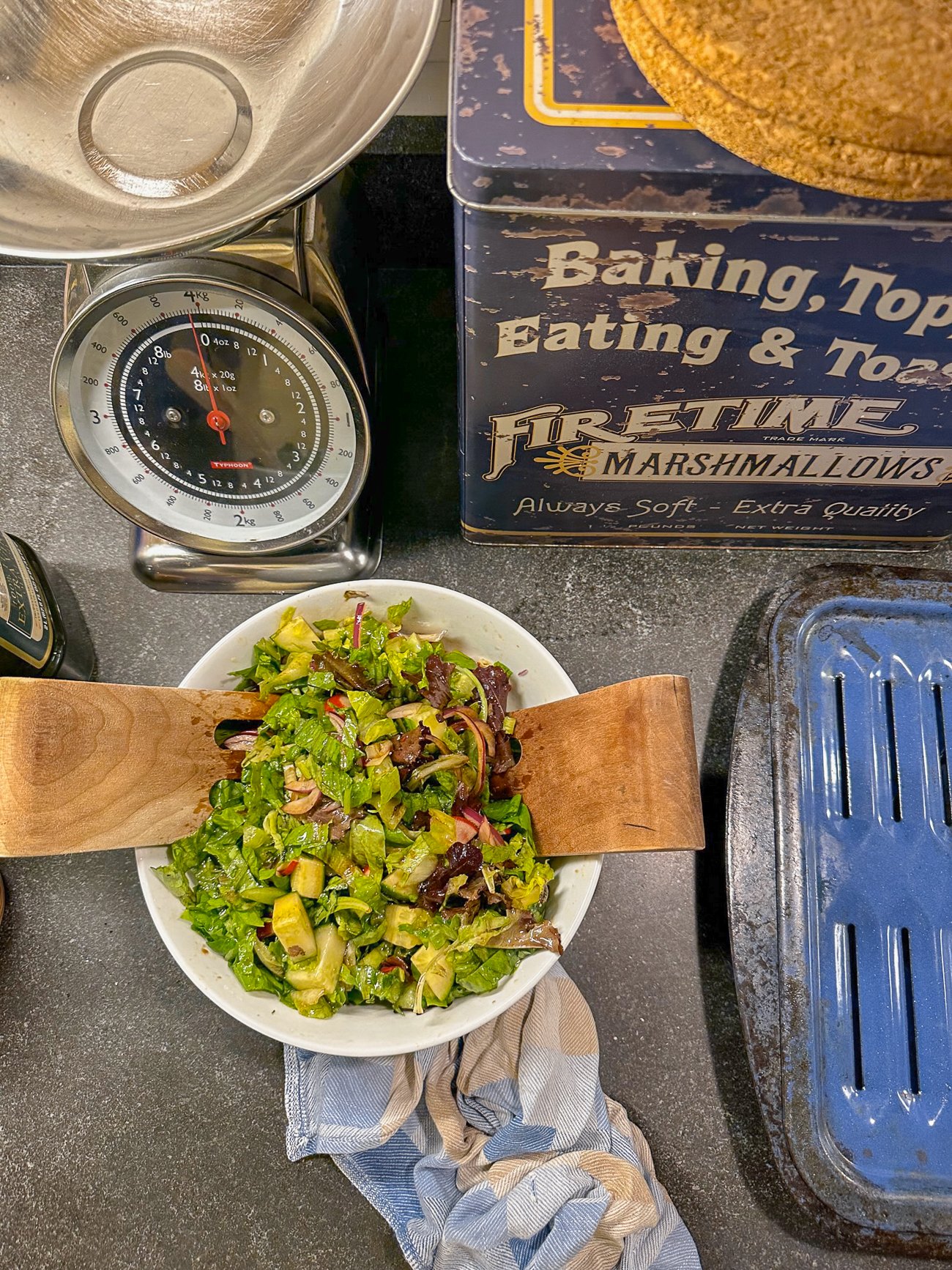 A salad on the counter with a Marshmallow tin and blue kitchen towel and blue metal baking pan