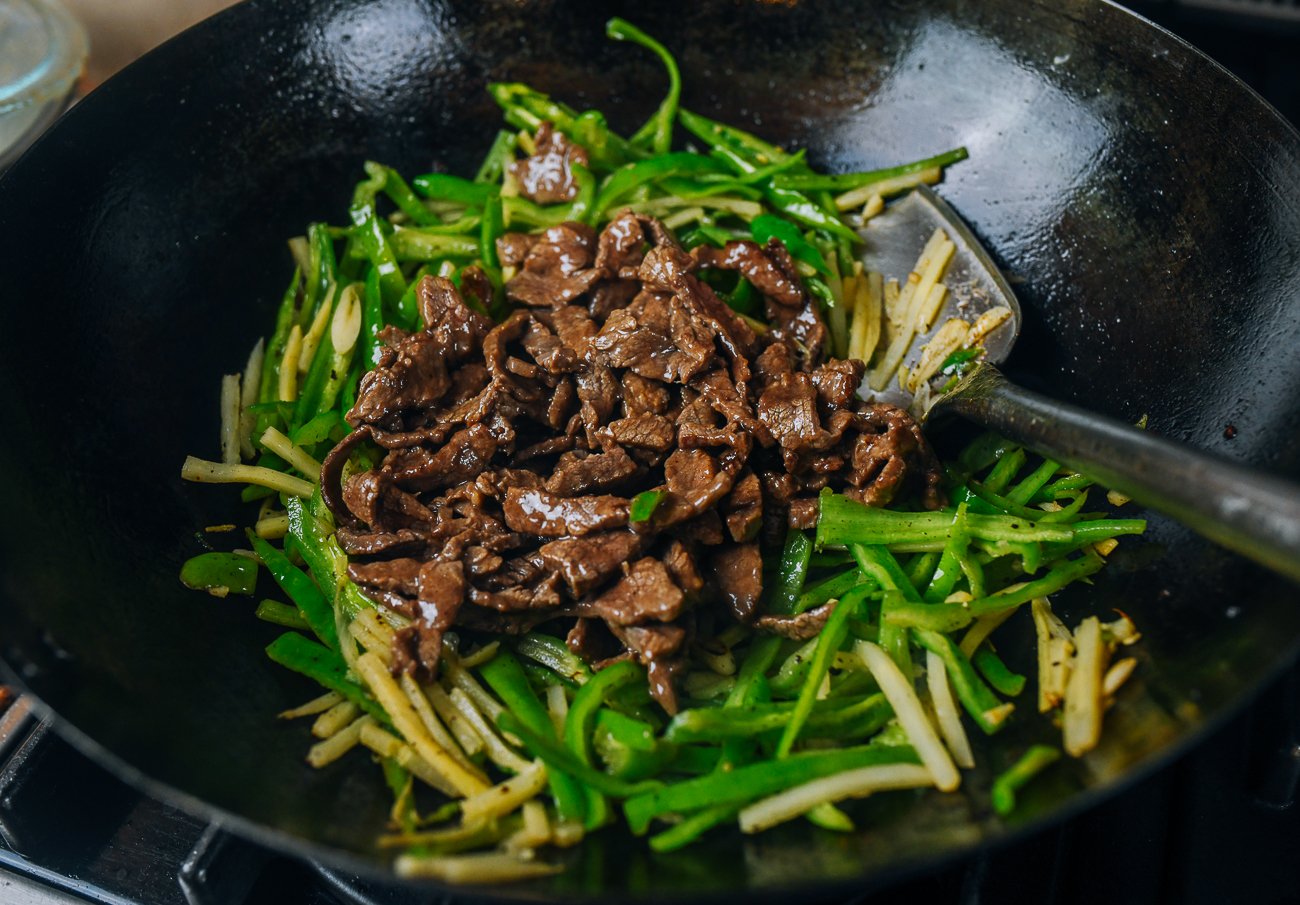 adding beef back to wok with bamboo shoots and peppers