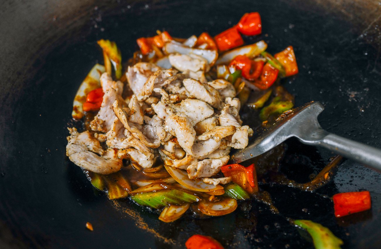 adding chicken to vegetables in wok