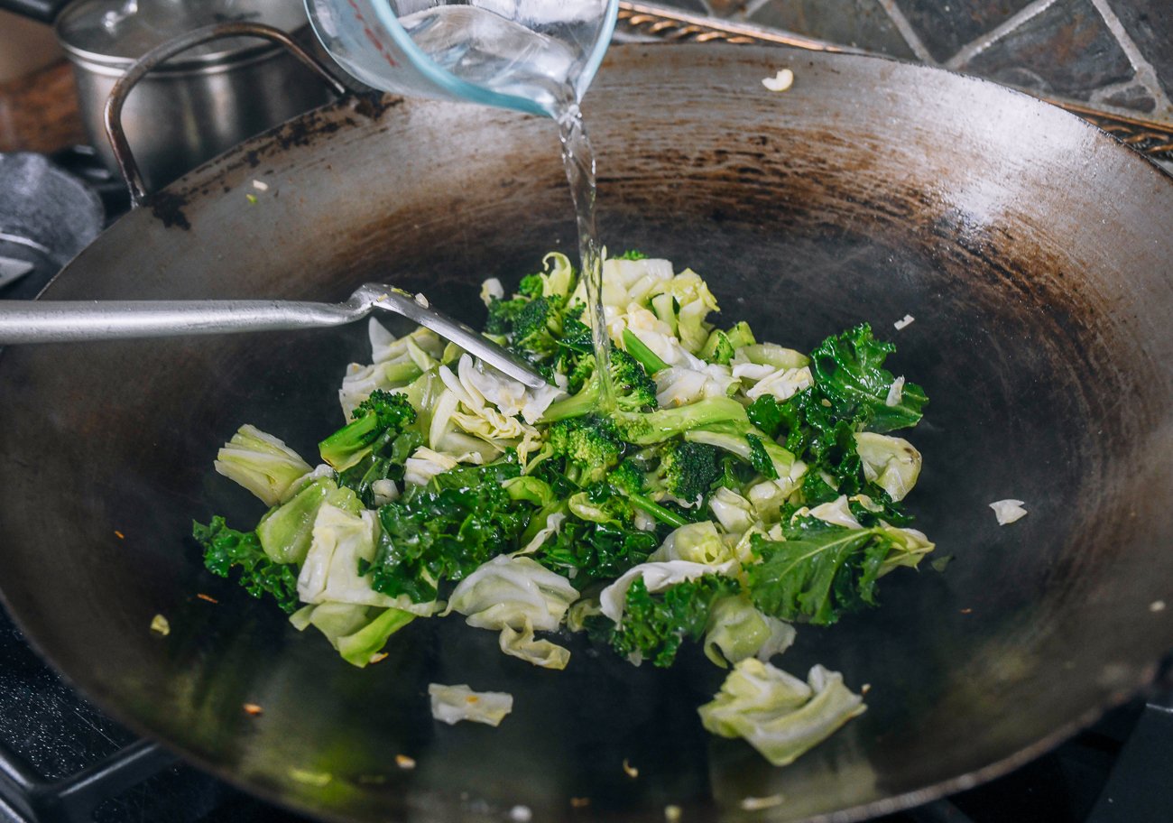 adding water to greens in wok