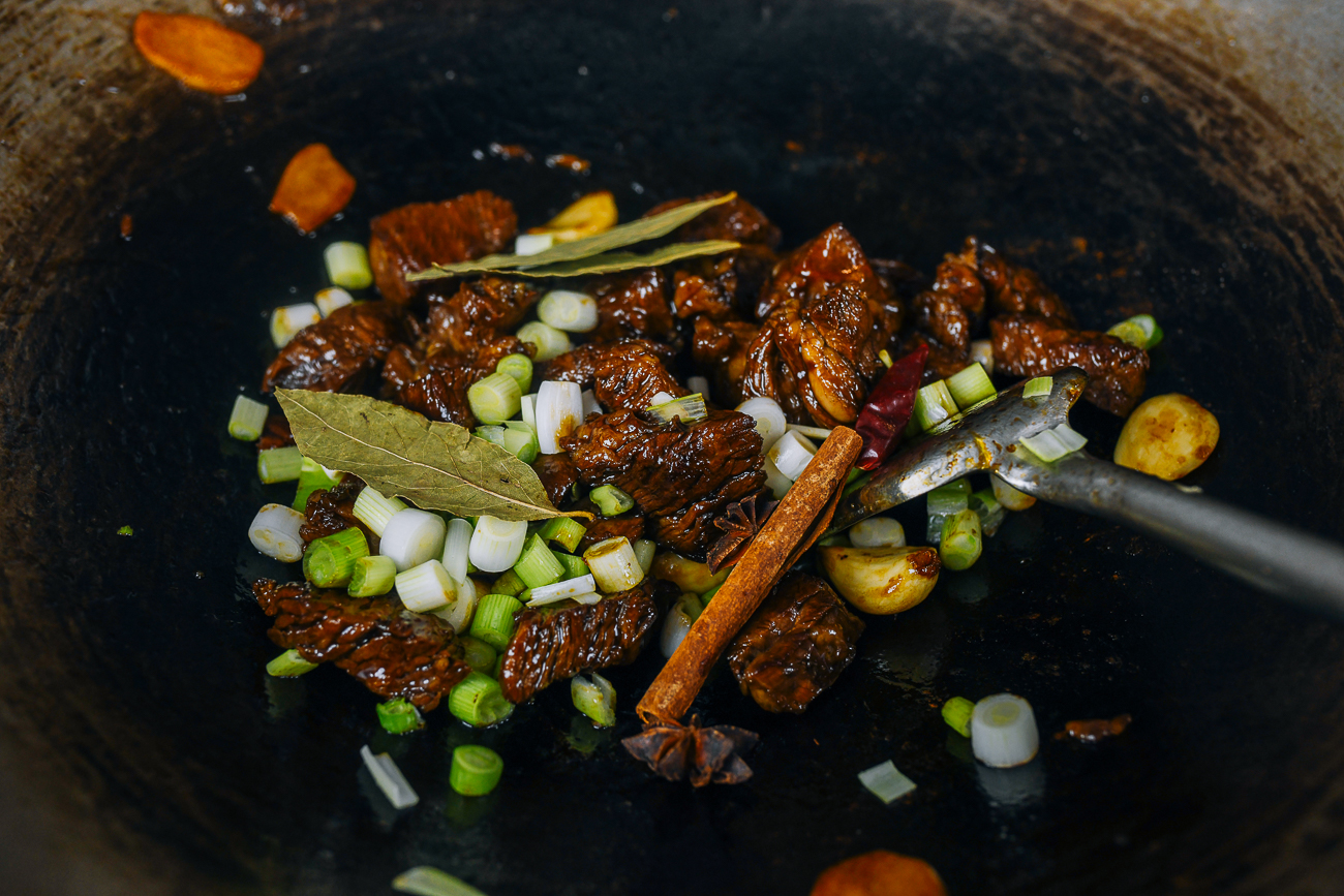 scallions, aromatics, and beef chunks in wok