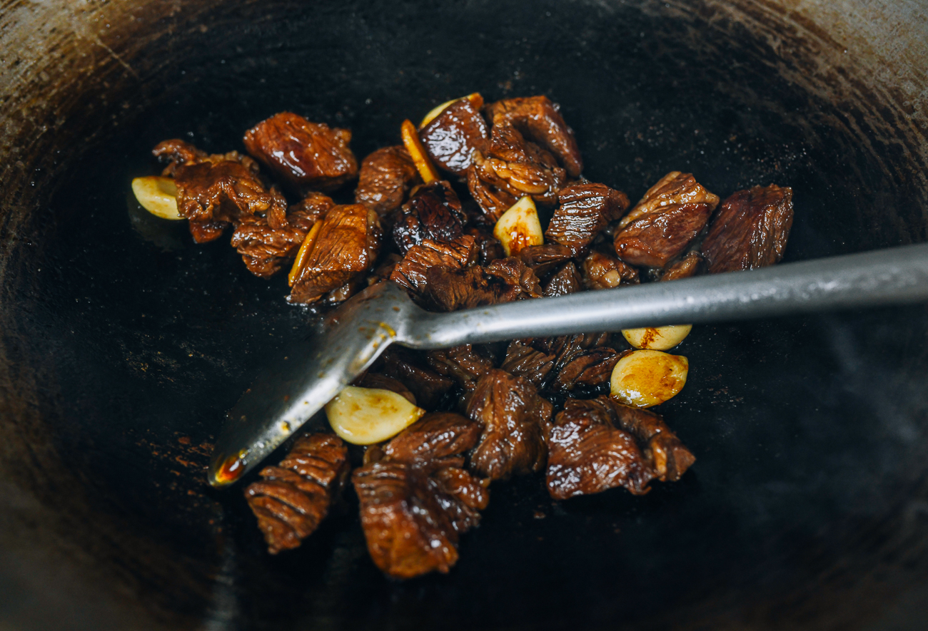 adding soy sauce to beef chunks in wok