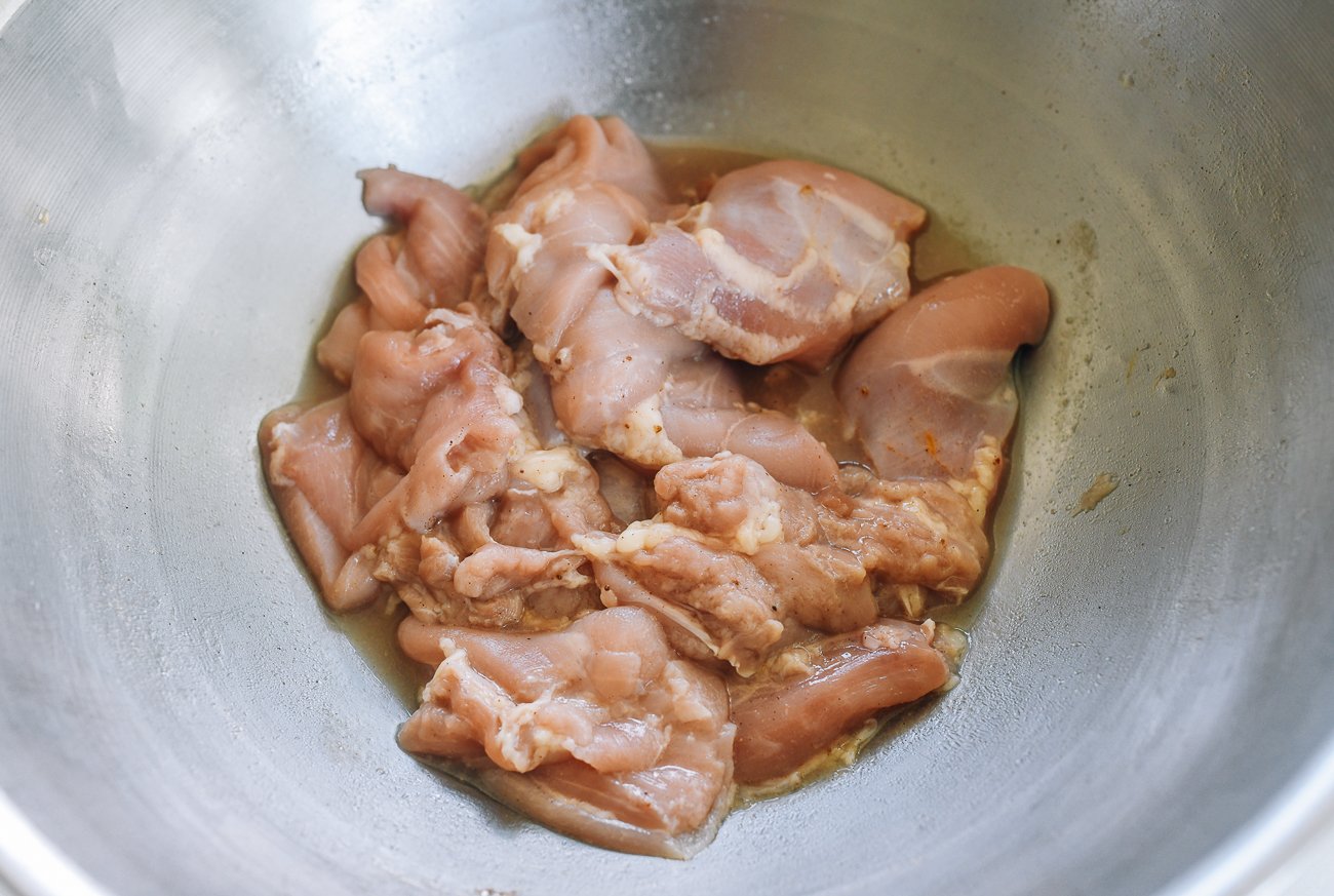 marinating boneless skinless chicken thigh pieces in metal bowl