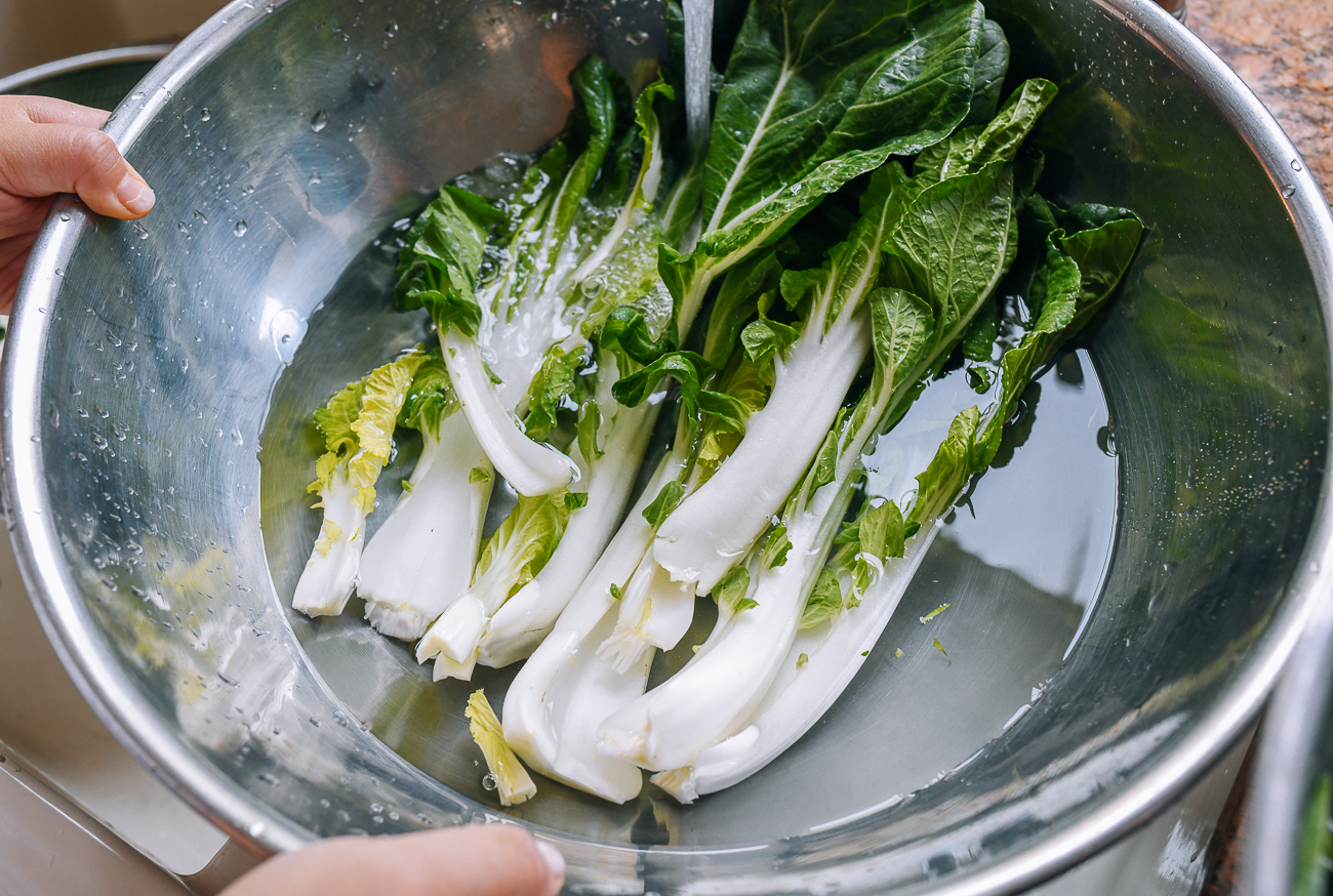 washing bok choy leaves in metal bowl with water