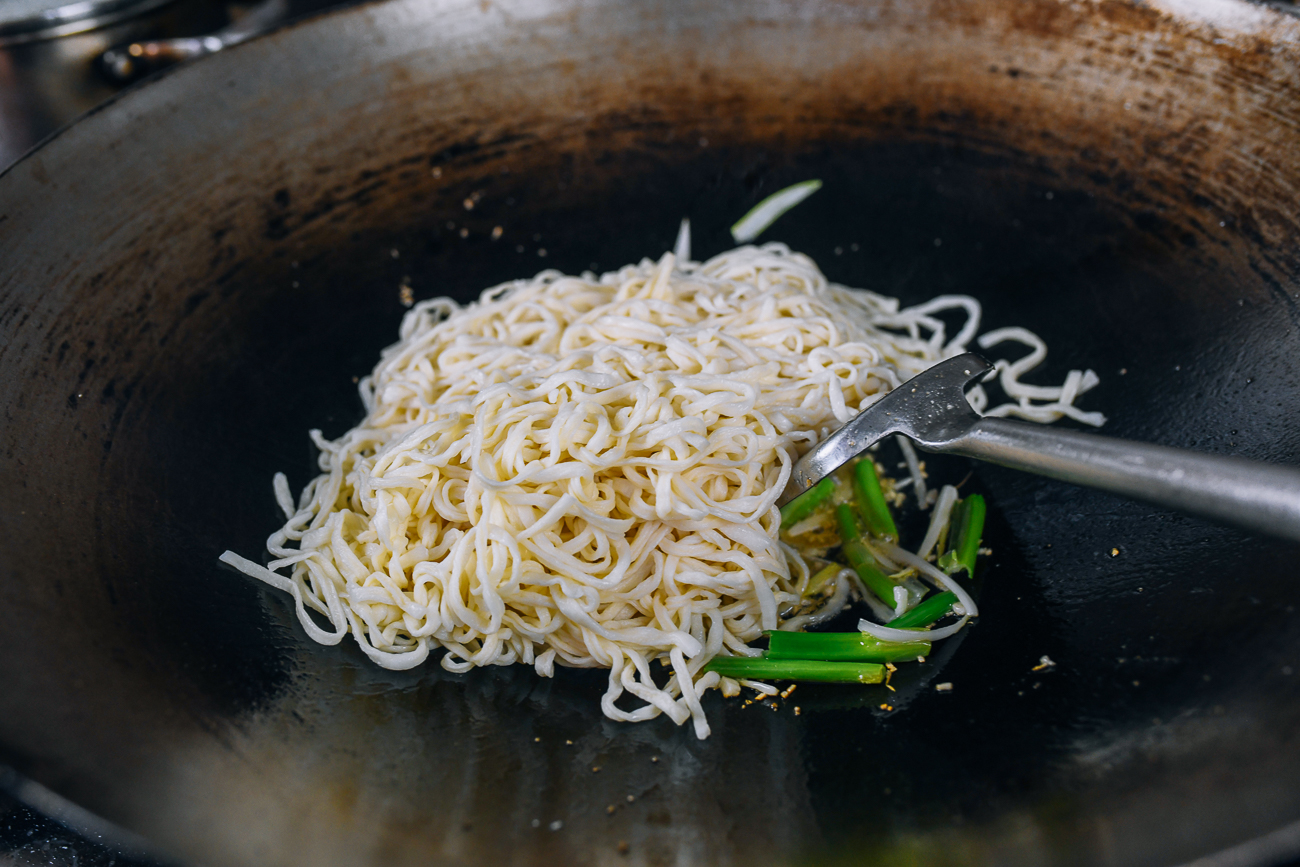 adding boiled e-fu noodles to wok with scallion and garlic