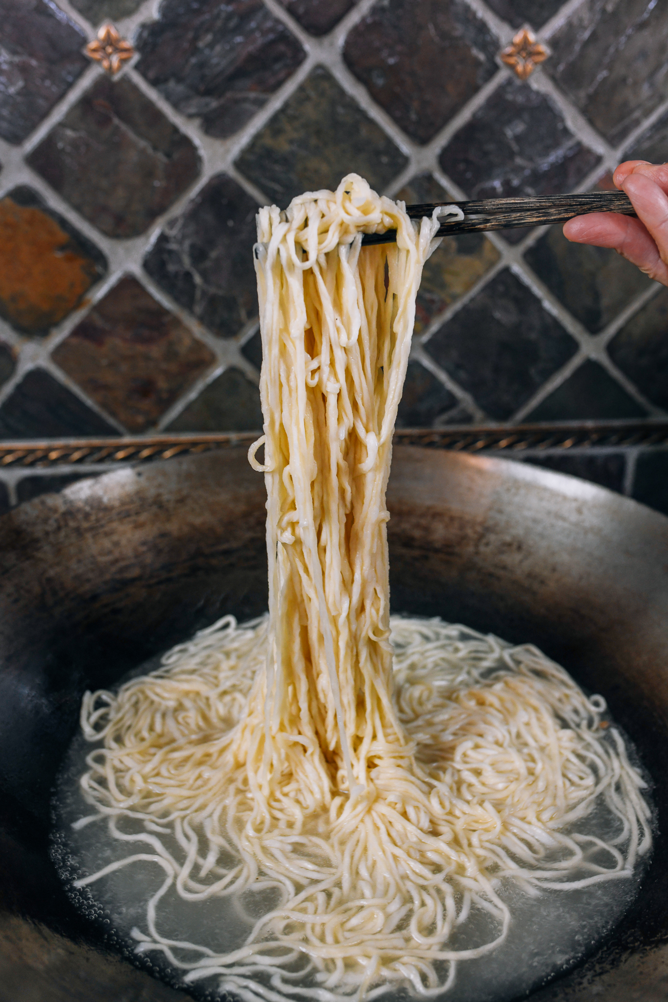 lifting cooked e-fu noodles (yee mein) out of boiling water