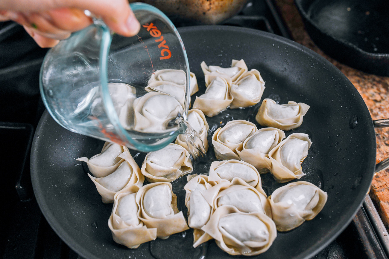 adding water to steam wontons in pan