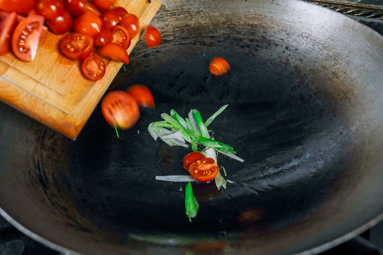 Adding tomatoes to scallion in wok