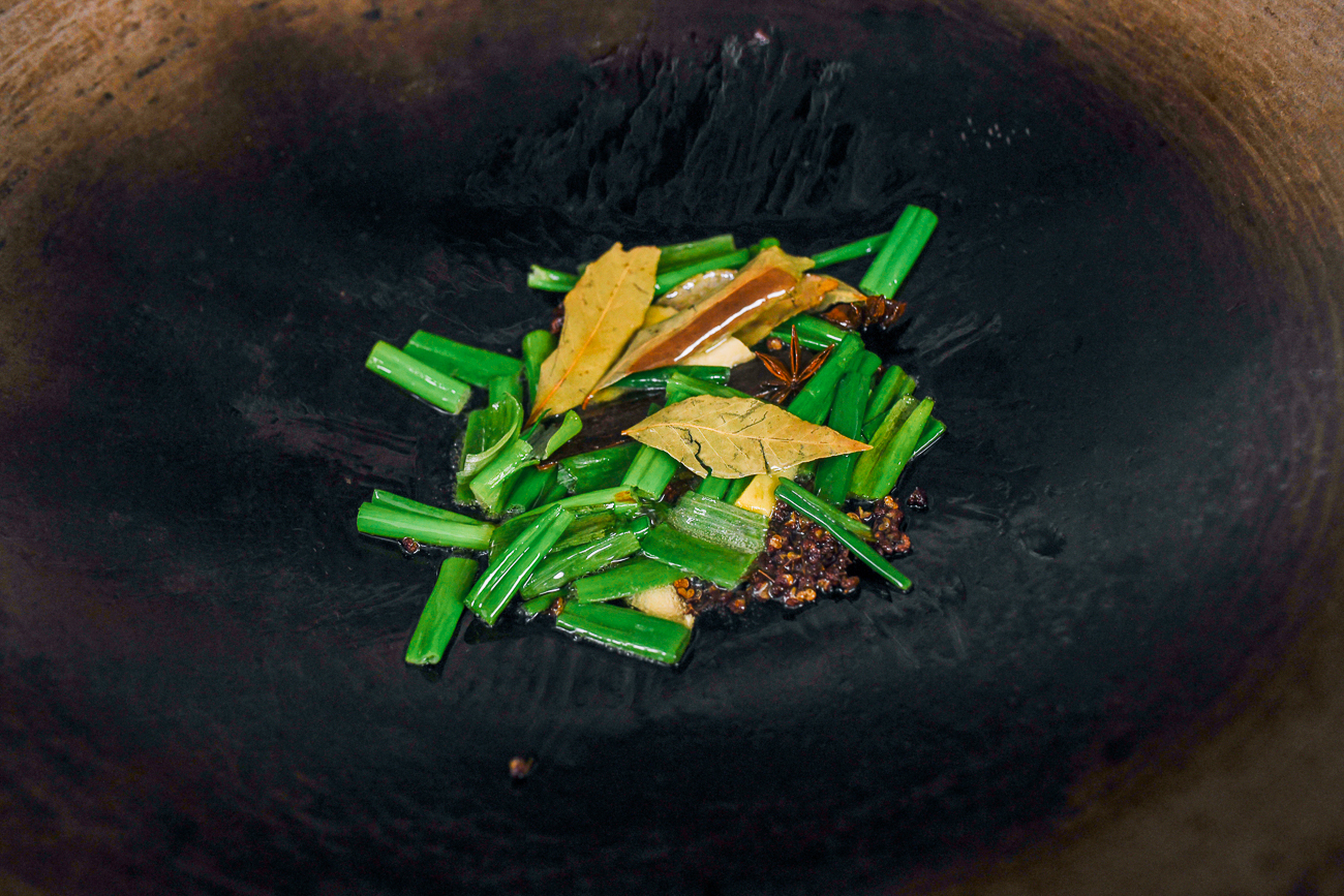 scallions, bay leaves and spices in wok with oil