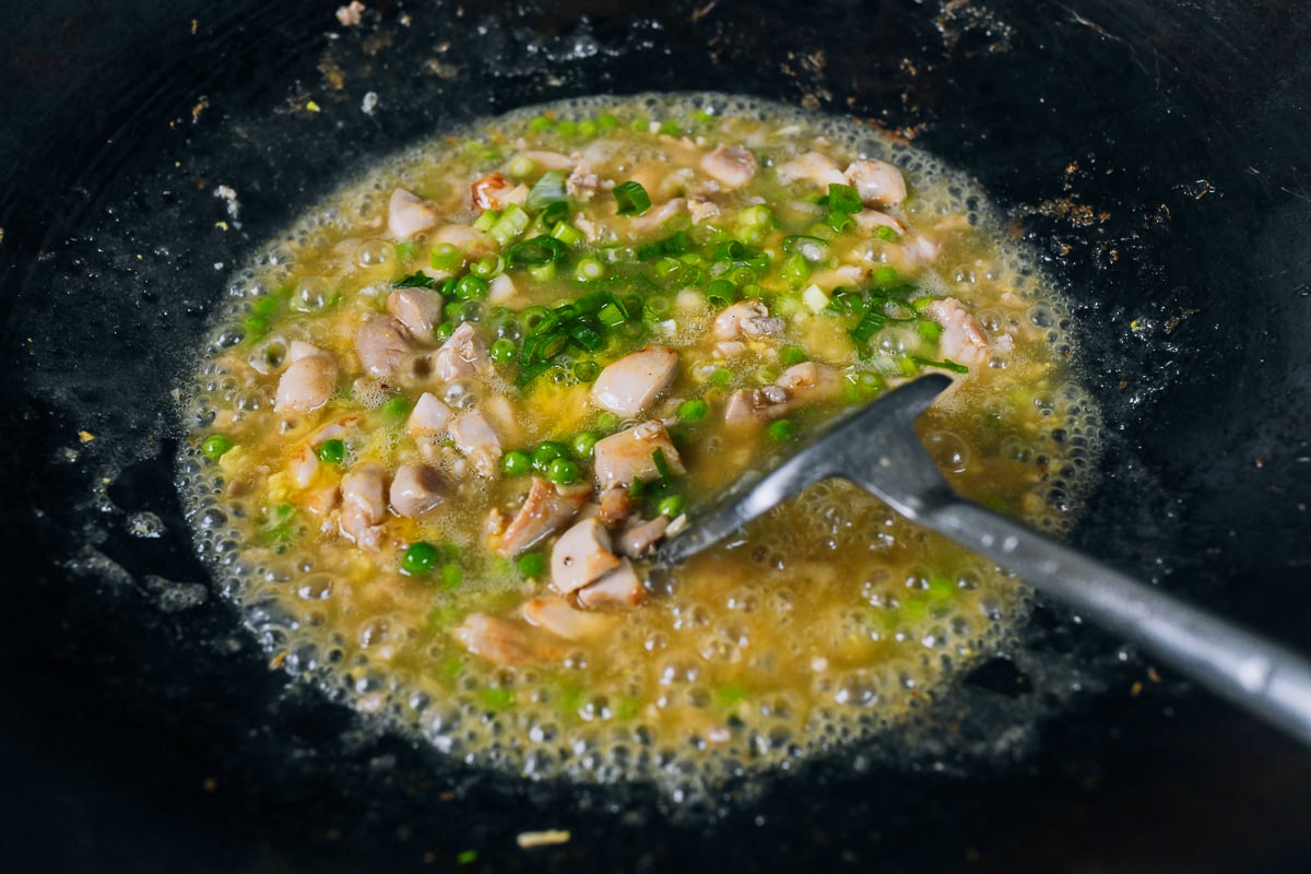 adding egg and scallions to chicken and sauce in wok