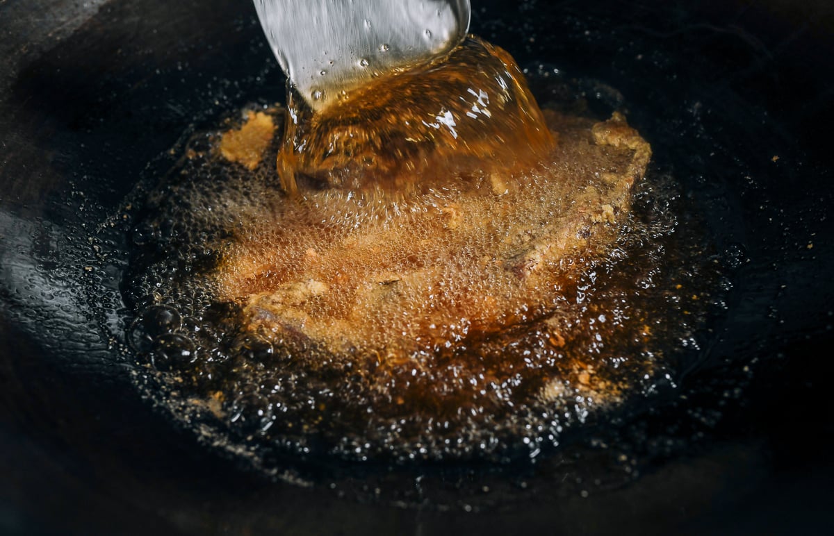 scooping hot oil onto pressed duck while frying