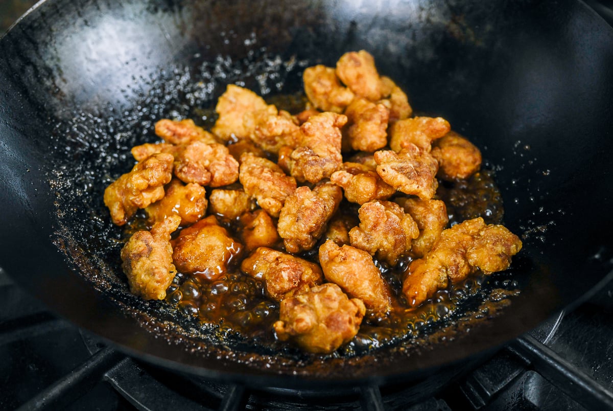 fried chicken pieces added to sauce in wok