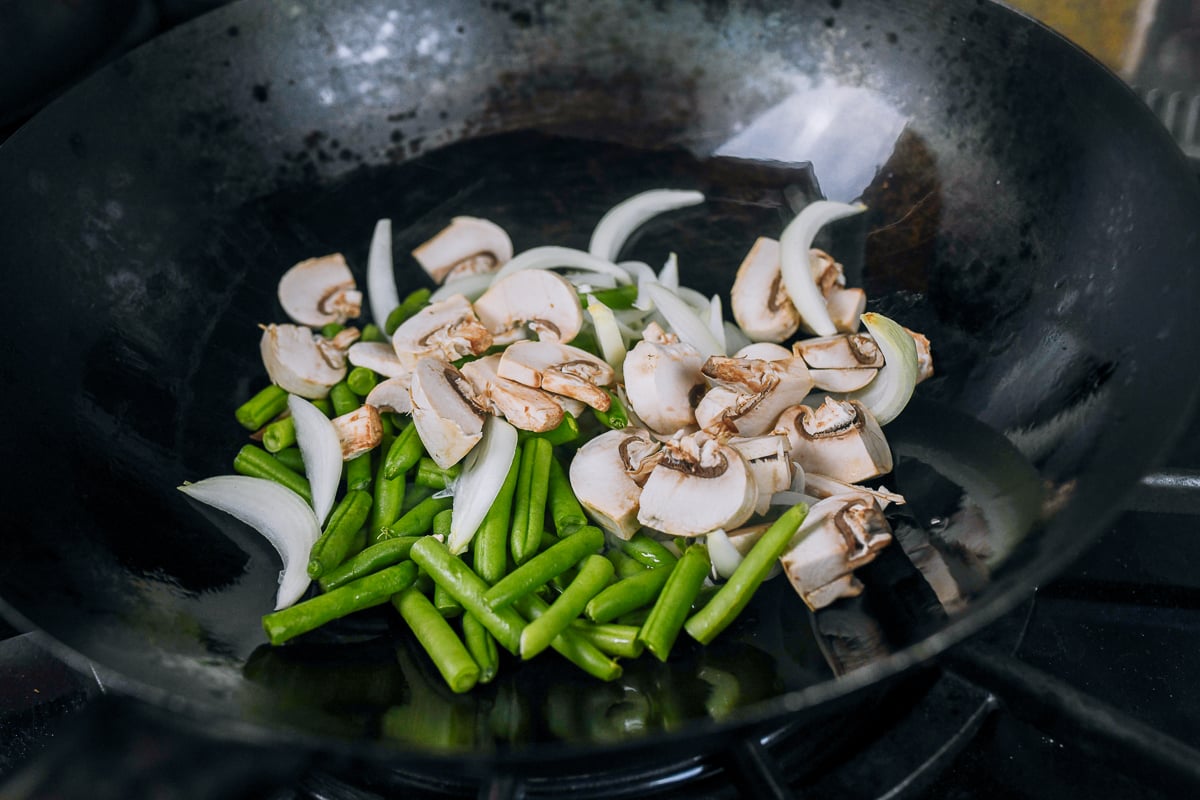 stir-frying green beans, onions, and mushrooms in wok