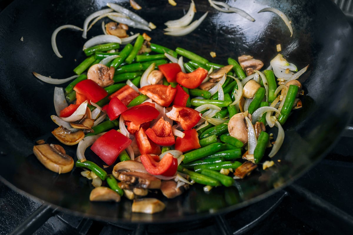 adding red bell pepper to vegetables in wok