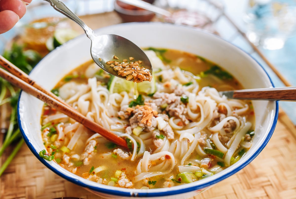 pouring garlic oil over tom yum noodle soup