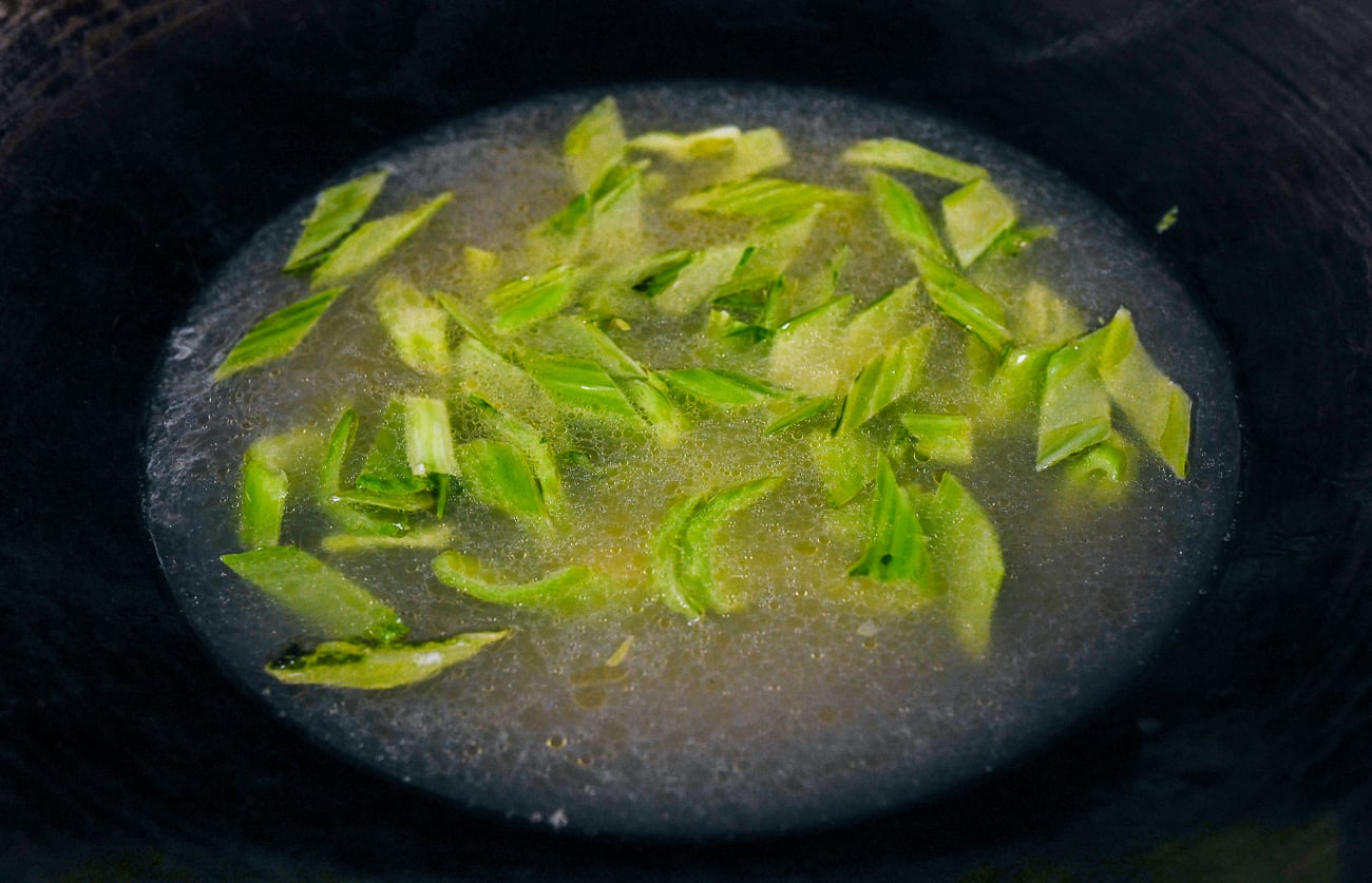chicken stock added to mustard greens in wok