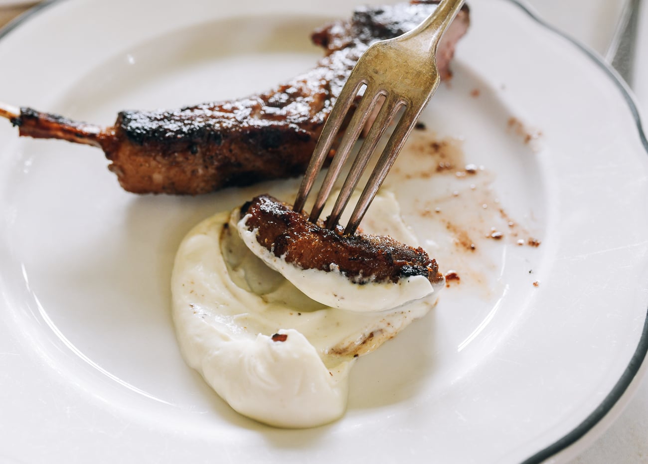 dipping grilled lamb chop into toum